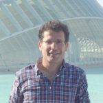Daniel Sola Man in front of a contruction in a checked shirt and glasses smiling to the camera